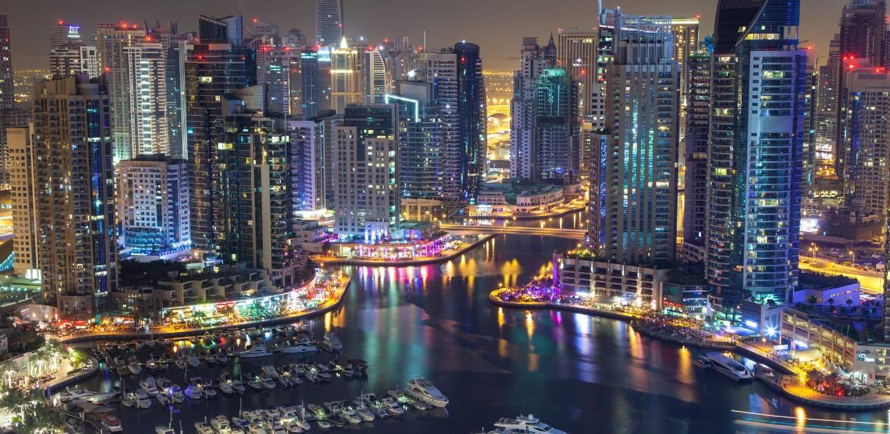 Night view of Dubai Marina skyline with illuminated buildings and waterfront, representing business growth and opportunities in Hamriyah Free Zone.