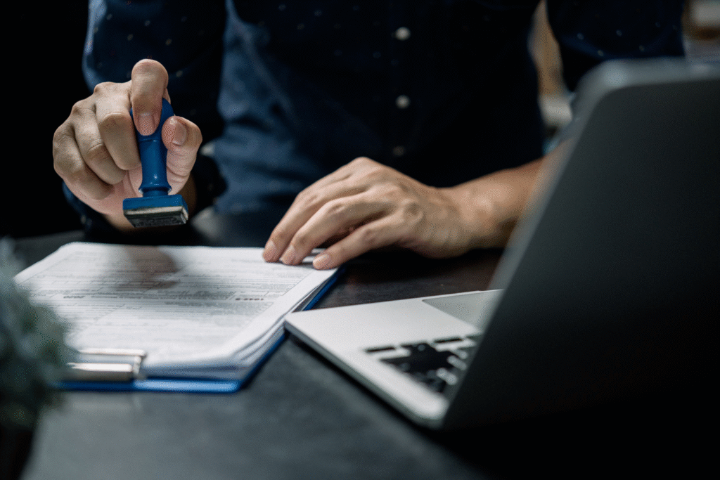 Person stamping official documents beside a laptop, representing efficient and reliable Labour and Immigration Services for businesses in the UAE.